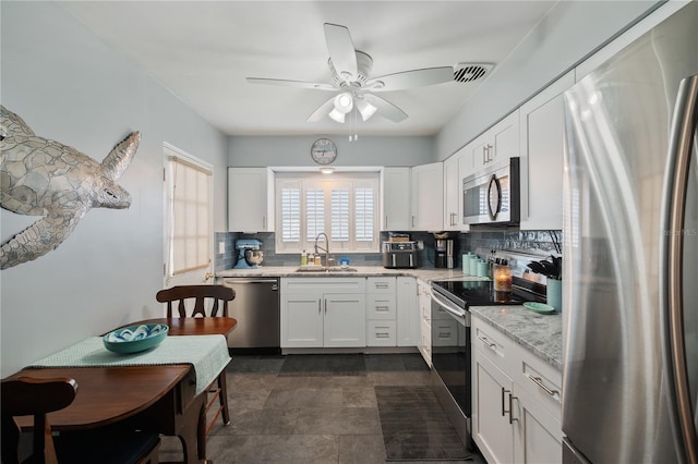 kitchen with tasteful backsplash, appliances with stainless steel finishes, light stone counters, white cabinetry, and a sink