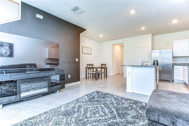 kitchen with dark stone countertops, visible vents, stainless steel fridge with ice dispenser, white cabinets, and open floor plan