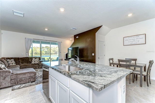 kitchen featuring visible vents, light stone countertops, open floor plan, white cabinetry, and a sink