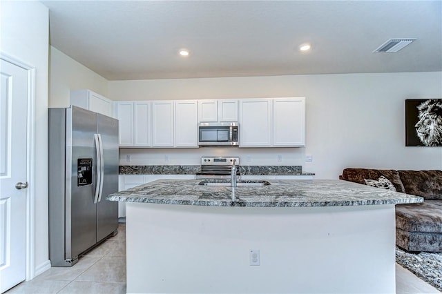 kitchen with a sink, white cabinetry, appliances with stainless steel finishes, stone counters, and light tile patterned floors