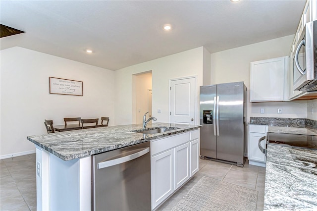 kitchen featuring a center island with sink, a sink, white cabinetry, appliances with stainless steel finishes, and stone counters