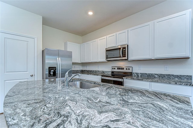 kitchen with a sink, white cabinetry, recessed lighting, stainless steel appliances, and dark stone counters