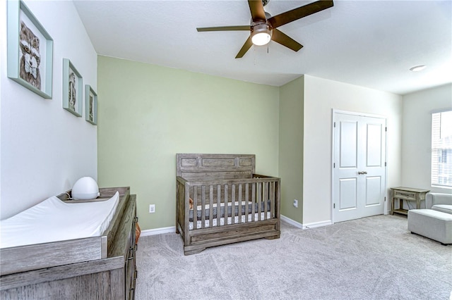 carpeted bedroom featuring a nursery area, baseboards, and ceiling fan