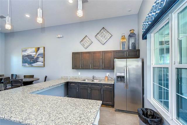 kitchen with dark brown cabinets, light stone countertops, a peninsula, stainless steel fridge, and a sink