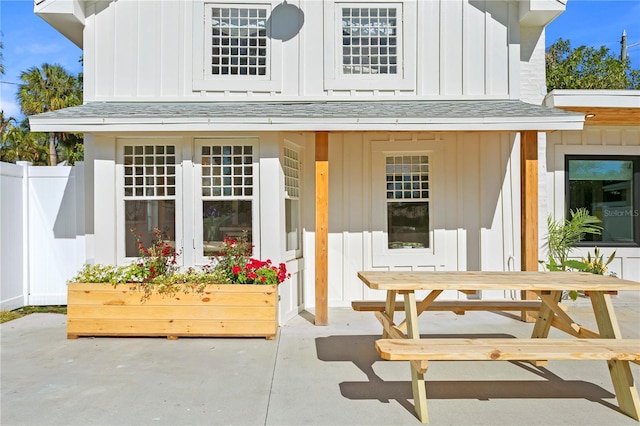 exterior space with board and batten siding, roof with shingles, and fence