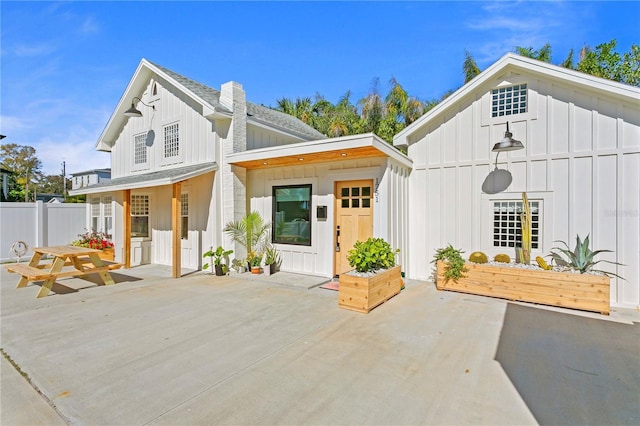 modern farmhouse featuring a shingled roof, board and batten siding, a patio area, and fence