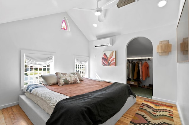 bedroom with arched walkways, high vaulted ceiling, wood finished floors, baseboards, and a wall mounted AC