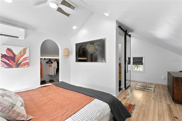 bedroom featuring a barn door, a ceiling fan, lofted ceiling, wood finished floors, and an AC wall unit