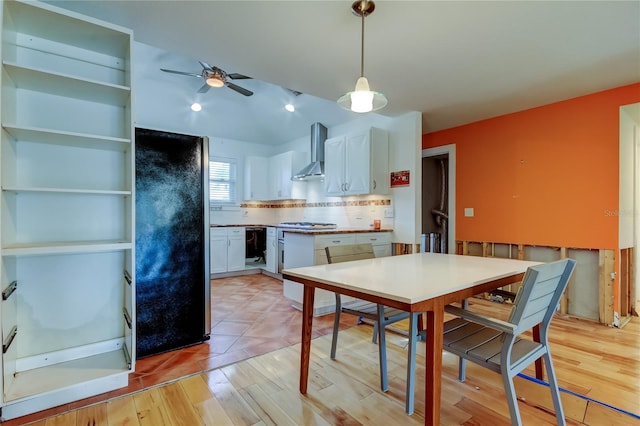 kitchen with wall chimney range hood, white cabinets, tasteful backsplash, and light wood finished floors