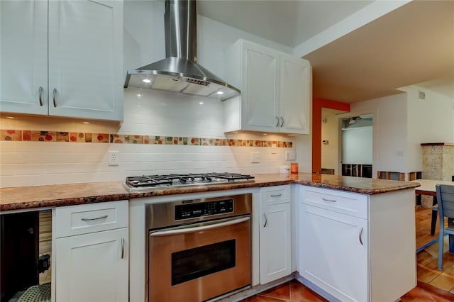 kitchen featuring backsplash, appliances with stainless steel finishes, wall chimney exhaust hood, white cabinets, and a peninsula