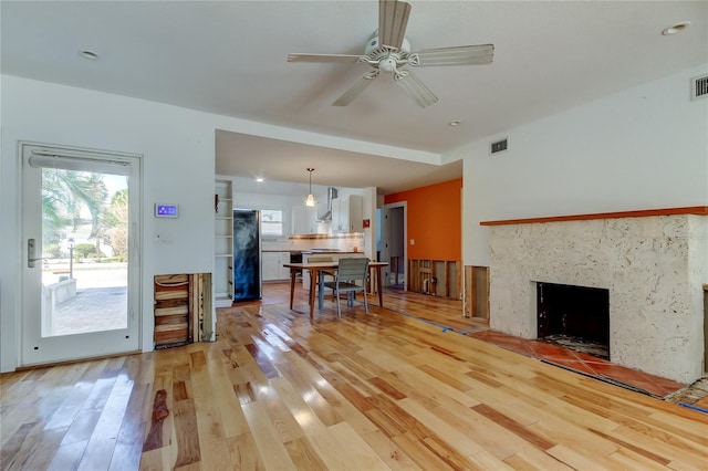 living area featuring light wood-type flooring, visible vents, and a fireplace