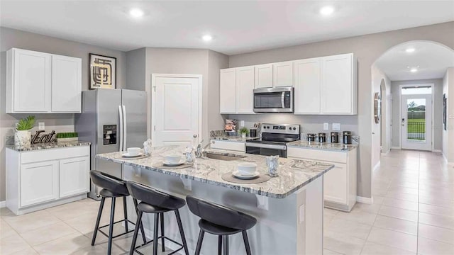 kitchen with light stone countertops, a kitchen bar, appliances with stainless steel finishes, and arched walkways