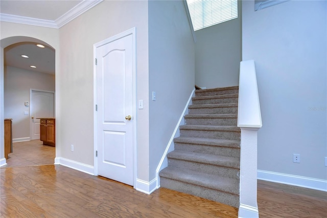 stairs with baseboards, arched walkways, wood finished floors, crown molding, and recessed lighting