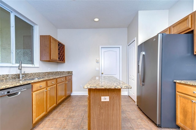 kitchen with a sink, appliances with stainless steel finishes, light tile patterned floors, and a kitchen island