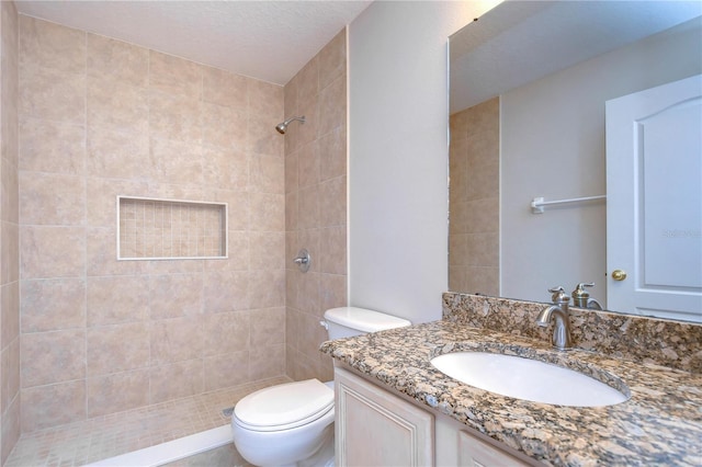 bathroom featuring vanity, a tile shower, and toilet