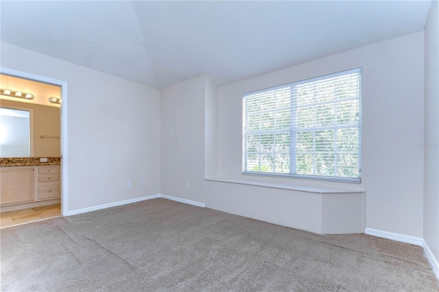 unfurnished bedroom with light carpet, ensuite bathroom, and baseboards