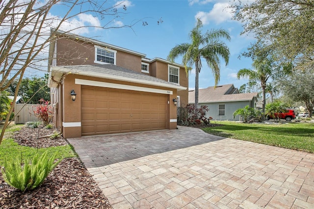 traditional-style house with a garage, fence, decorative driveway, a front lawn, and stucco siding