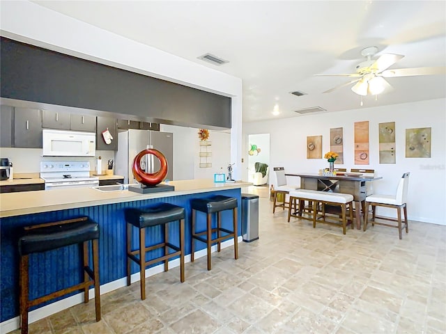 kitchen with visible vents, ceiling fan, a breakfast bar area, light countertops, and white appliances