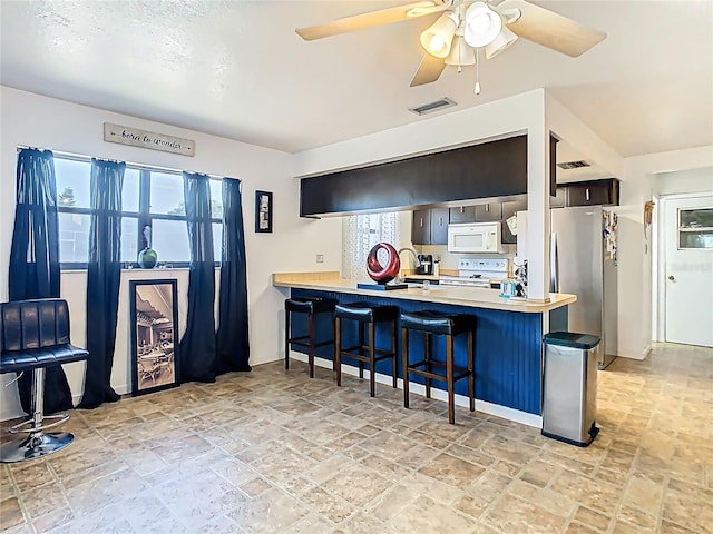 kitchen featuring visible vents, a kitchen bar, light countertops, a peninsula, and white appliances