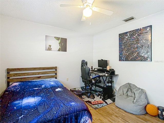 bedroom with visible vents, a textured ceiling, wood finished floors, and a ceiling fan