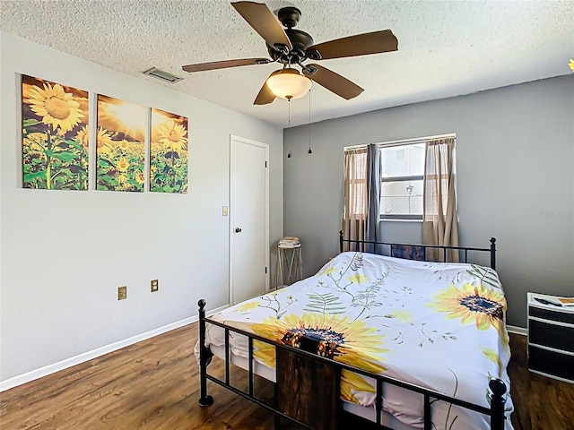 bedroom featuring visible vents, a textured ceiling, wood finished floors, baseboards, and ceiling fan