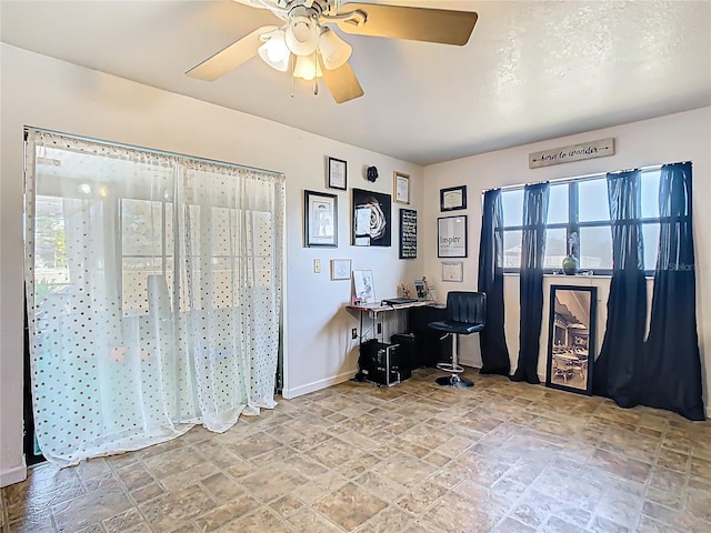 office area with ceiling fan, stone finish flooring, and baseboards