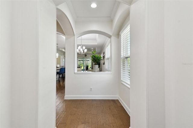 hallway with a notable chandelier, ornamental molding, wood finished floors, arched walkways, and baseboards