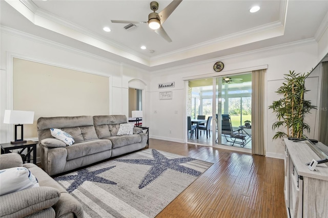 living room featuring a raised ceiling, arched walkways, and dark wood finished floors