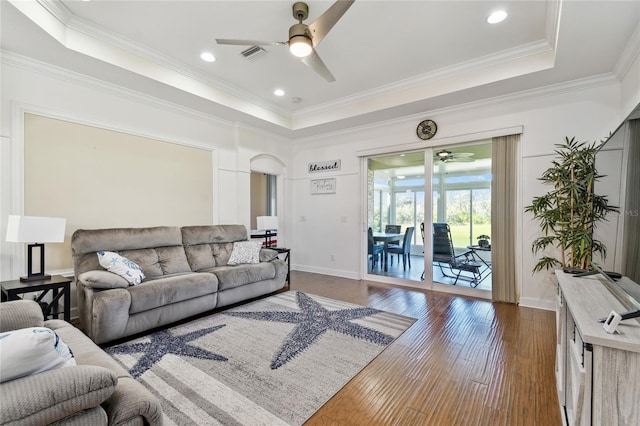 living area featuring a tray ceiling, dark wood finished floors, arched walkways, crown molding, and baseboards