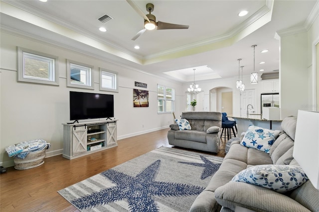 living area with wood finished floors, visible vents, a tray ceiling, arched walkways, and ornamental molding