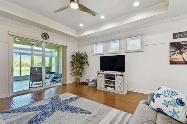 living room with baseboards, a raised ceiling, wood finished floors, and crown molding