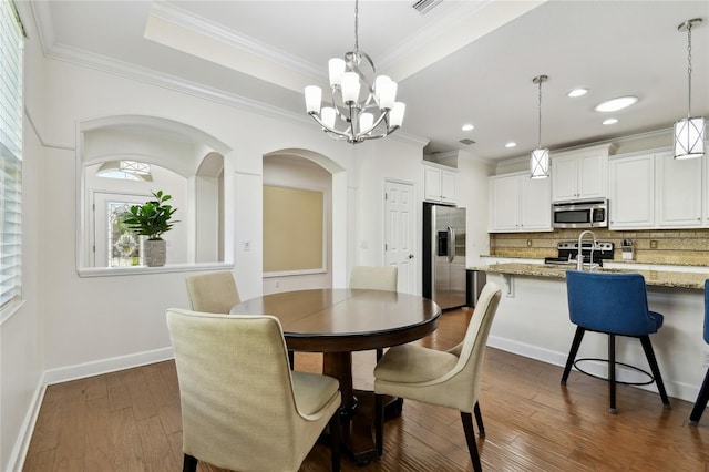 dining space featuring a notable chandelier, a tray ceiling, dark wood-style floors, crown molding, and baseboards