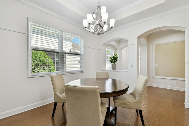 dining space featuring wood finished floors, baseboards, a tray ceiling, crown molding, and a notable chandelier