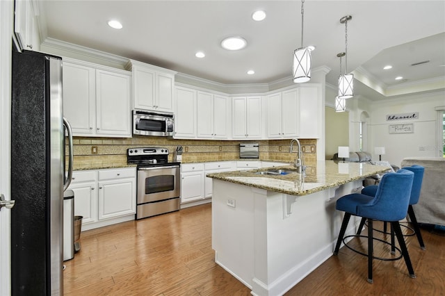 kitchen with white cabinets, light wood-style floors, appliances with stainless steel finishes, a kitchen bar, and crown molding