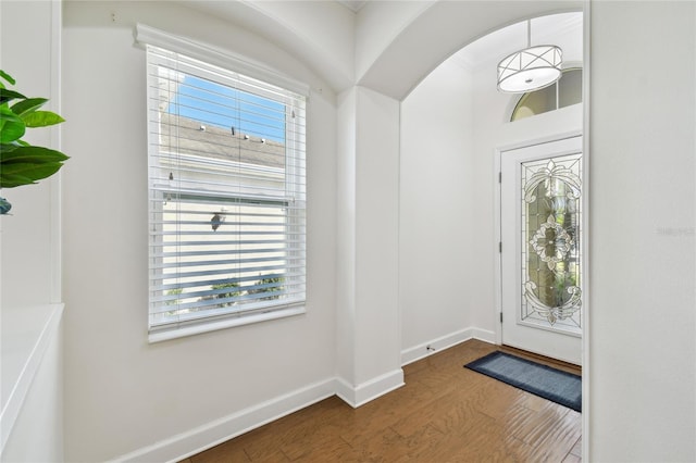 foyer featuring dark wood-style floors, arched walkways, and baseboards