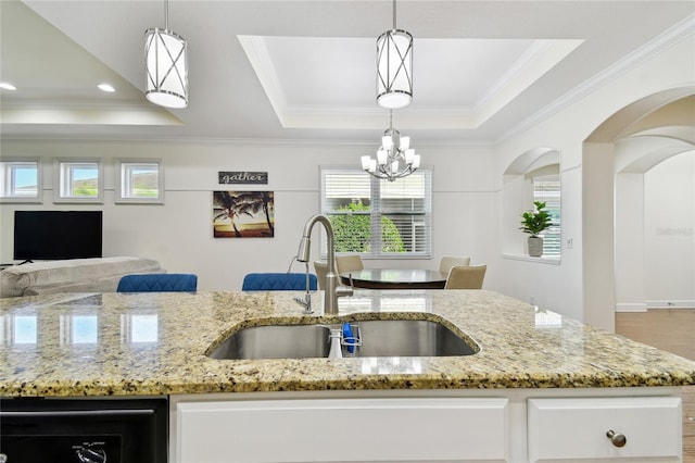 kitchen featuring light stone countertops, a tray ceiling, an inviting chandelier, white cabinetry, and a sink