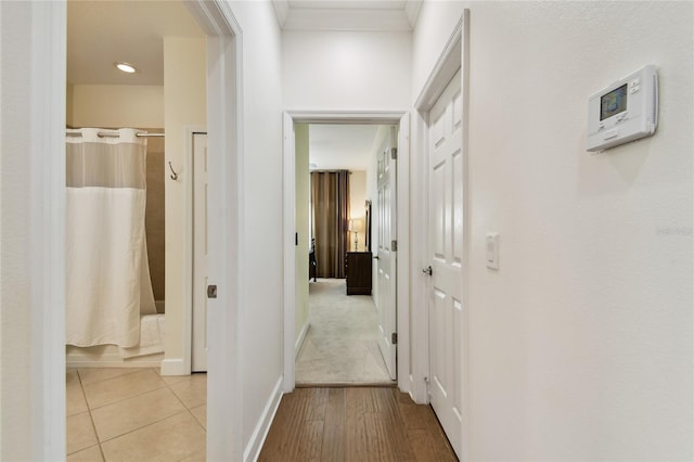 hall featuring light wood-type flooring, crown molding, and baseboards