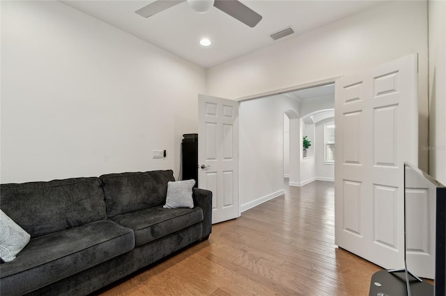 living area with light wood-type flooring, visible vents, arched walkways, baseboards, and ceiling fan