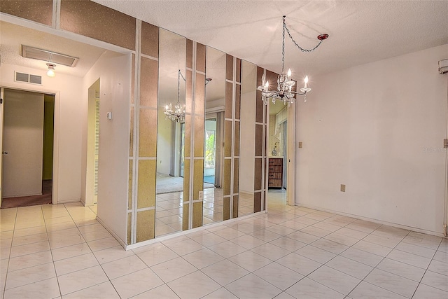 spare room featuring a notable chandelier, light tile patterned flooring, visible vents, and a textured ceiling