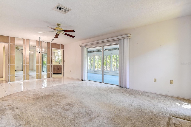 carpeted empty room with tile patterned flooring, ceiling fan with notable chandelier, visible vents, and a textured ceiling