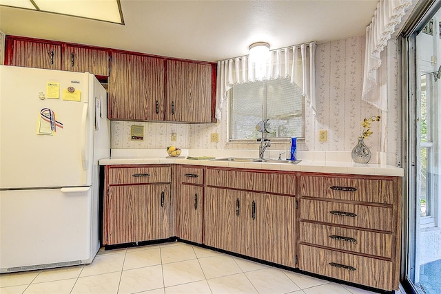 kitchen featuring wallpapered walls, a wealth of natural light, freestanding refrigerator, and a sink