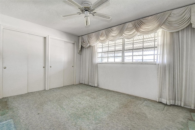 unfurnished bedroom featuring a ceiling fan, multiple closets, carpet floors, and a textured ceiling