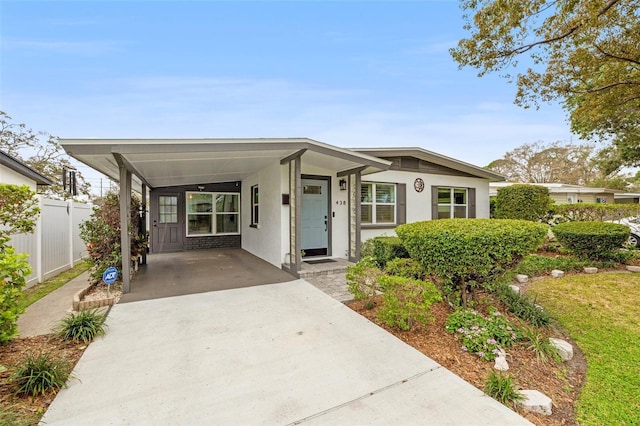 view of front of house with driveway, a carport, fence, and stucco siding