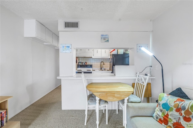 kitchen featuring light colored carpet, under cabinet range hood, a peninsula, visible vents, and freestanding refrigerator