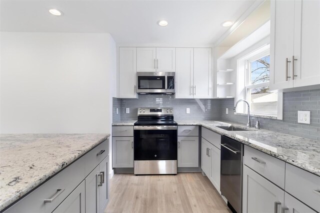 kitchen with backsplash, appliances with stainless steel finishes, light wood-style floors, a sink, and light stone countertops