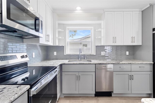 kitchen featuring open shelves, light stone counters, stainless steel appliances, and a sink