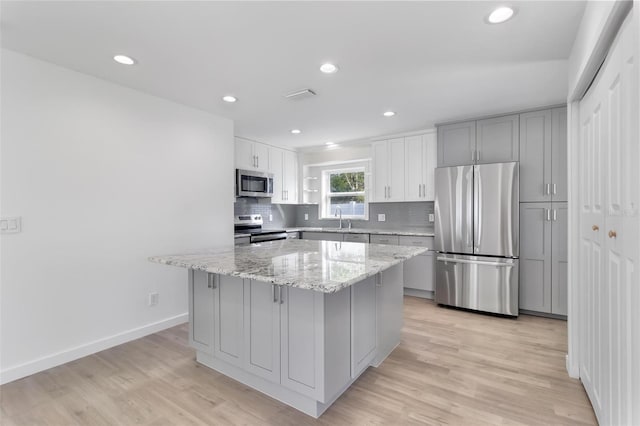 kitchen with light wood finished floors, a kitchen island, appliances with stainless steel finishes, and decorative backsplash