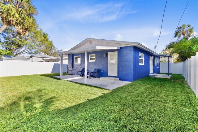 rear view of house featuring concrete block siding, a fenced backyard, a lawn, and a patio