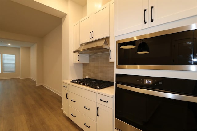 kitchen featuring under cabinet range hood, wood finished floors, white cabinets, appliances with stainless steel finishes, and tasteful backsplash