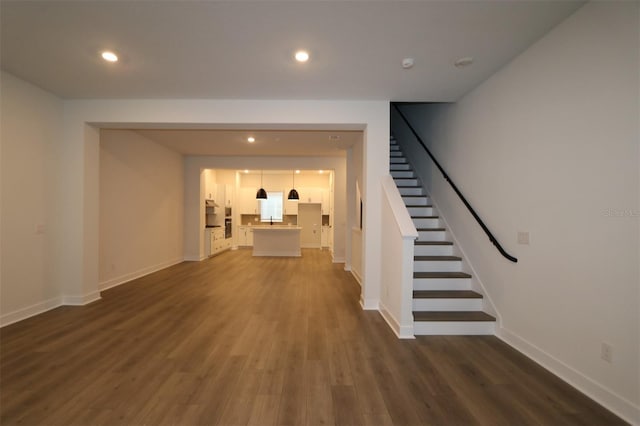 unfurnished living room with dark wood-type flooring, recessed lighting, baseboards, and stairs